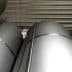 Several large silver storage tanks stacked closely together in a warehouse setting. - Olive Oil Times