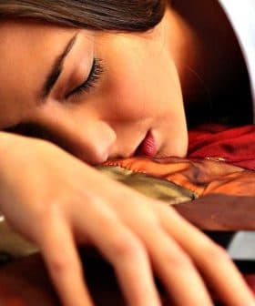 A woman resting her head on a bed with her arm extended towards a smartphone. - Olive Oil Times