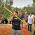 Group of people observing an olive harvesting demonstration with a worker using a pole. - Olive Oil Times