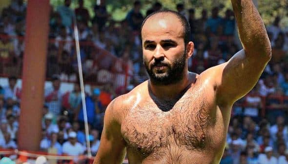 A shirtless male competitor in traditional Turkish oil wrestling raising his arm in victory. - Olive Oil Times
