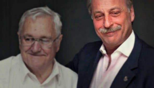 Two men standing close together, smiling for a photograph in a dimly lit setting. - Olive Oil Times