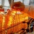 A person holding a bottle of cooking oil on a production line with multiple bottles in the background. - Olive Oil Times