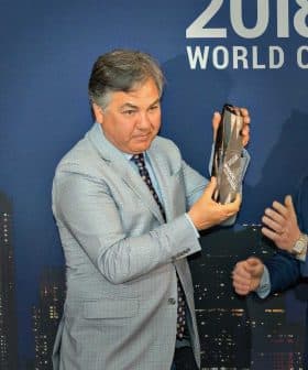 Two men at an award ceremony, one presenting a bottle to the other in front of a city skyline backdrop. - Olive Oil Times