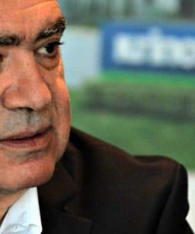 Man with gray hair wearing a black suit and white shirt, seated and looking to the side. - Olive Oil Times