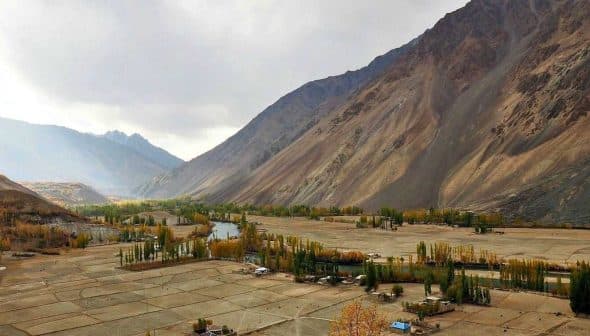 A panoramic view of a mountainous landscape featuring fields and a river in the foreground. - Olive Oil Times