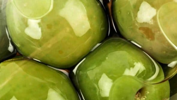 Close-up of green olives submerged in brine with a glossy surface. - Olive Oil Times