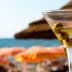A martini glass filled with a clear liquid and three green olives, with a beach background. - Olive Oil Times