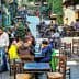 Outdoor dining area featuring wooden tables and chairs in a bustling setting with patrons. - Olive Oil Times