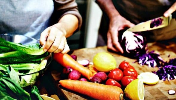 Hands preparing vegetables including lettuce, carrots, tomatoes, and cabbage on a wooden cutting board. - Olive Oil Times