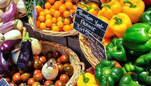 A display of various fresh vegetables and fruits including peppers, tomatoes, and eggplants in baskets. - Olive Oil Times