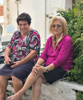 Five elderly individuals sitting on a stone wall in a village setting, with greenery in the background. - Olive Oil Times