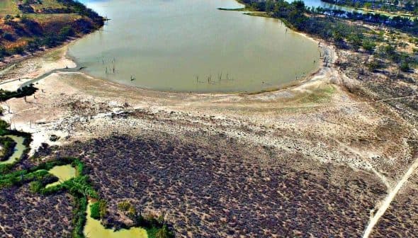 Aerial image showing a dry lakebed with patches of green vegetation and a winding waterway. - Olive Oil Times