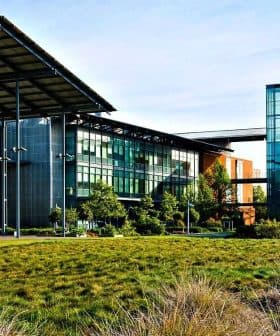 Modern building featuring a combination of glass and orange exterior elements with a landscaped area in front. - Olive Oil Times