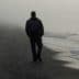 Individual walking alone on a foggy beach with gentle waves lapping at the shore. - Olive Oil Times