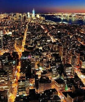 Aerial view of New York City skyline illuminated at night with city lights and buildings visible. - Olive Oil Times