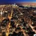 Aerial view of New York City skyline illuminated at night with city lights and buildings visible. - Olive Oil Times