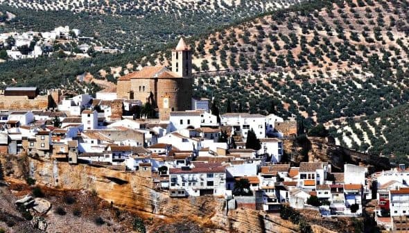 A panoramic view of a white village in Andalusia surrounded by olive groves on rolling hills. - Olive Oil Times