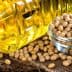 Transparent bottle of cooking oil next to a bowl of soybeans on a burlap surface. - Olive Oil Times