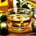 Glass container pouring olive oil into a small glass bowl with olives beside it. - Olive Oil Times