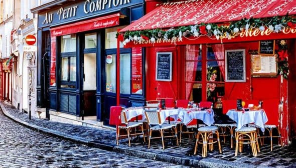 Outdoor café seating with tables and chairs arranged on a cobblestone street in Paris. - Olive Oil Times
