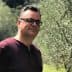 Man wearing glasses standing in an olive grove with trees in the background. - Olive Oil Times
