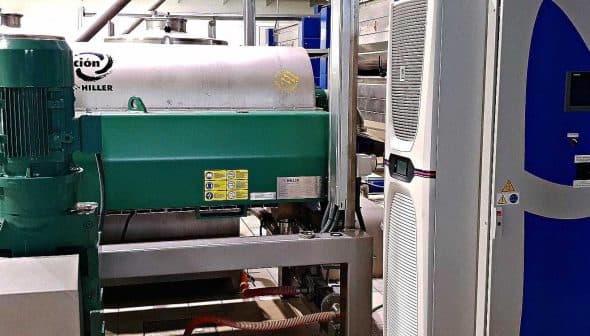 Industrial machinery used for olive oil processing, featuring a green motor and stainless steel tanks. - Olive Oil Times