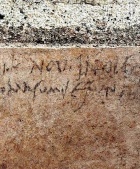 Faded ancient inscription carved into a stone wall with visible texture and cracks. - Olive Oil Times