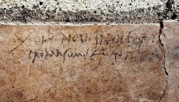 Faded ancient inscription carved into a stone wall with visible texture and cracks. - Olive Oil Times