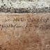 Faded ancient inscription carved into a stone wall with visible texture and cracks. - Olive Oil Times