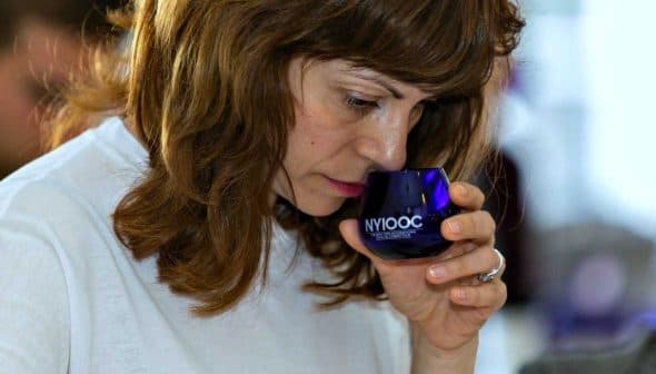 Woman with brown hair smelling olive oil from a blue glass container during a tasting event. - Olive Oil Times