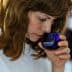 Woman with brown hair smelling olive oil from a blue glass container during a tasting event. - Olive Oil Times