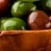 A wooden bowl filled with a variety of green and brown olives resting in oil. - Olive Oil Times