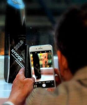 Individual capturing an image with a smartphone while seated near a window. - Olive Oil Times