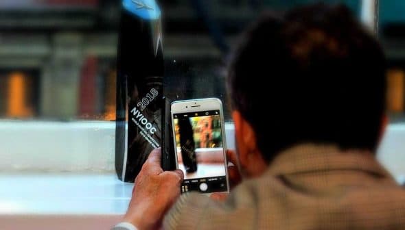 Individual capturing an image with a smartphone while seated near a window. - Olive Oil Times