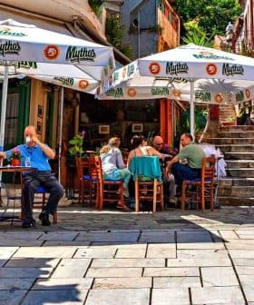 Outdoor café scene featuring patrons seated under large umbrellas in a narrow street. - Olive Oil Times