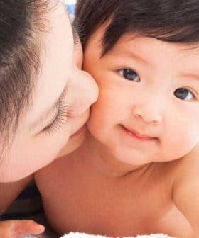 A mother kissing her baby on a soft surface, both looking at the camera. - Olive Oil Times