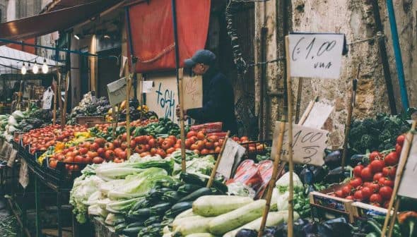 Market stall displaying various vegetables and fruits, including tomatoes, cucumbers, and leafy greens. - Olive Oil Times