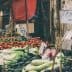 Market stall displaying various vegetables and fruits, including tomatoes, cucumbers, and leafy greens. - Olive Oil Times