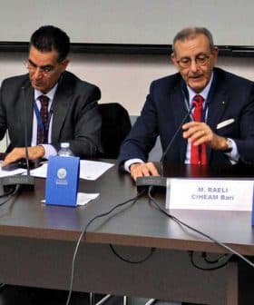 Four speakers seated at a table during a panel discussion, with microphones and name cards in front of them. - Olive Oil Times