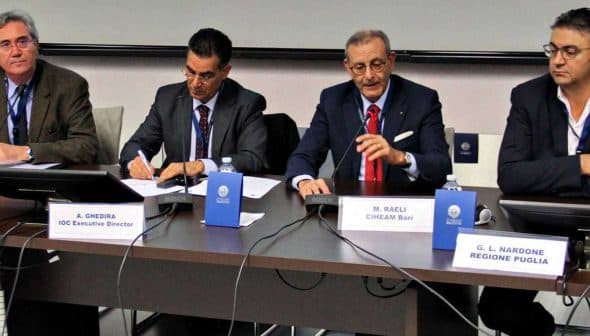 Four speakers seated at a table during a panel discussion, with microphones and name cards in front of them. - Olive Oil Times