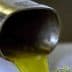 Stream of olive oil pouring from a metal spout into a container during production. - Olive Oil Times