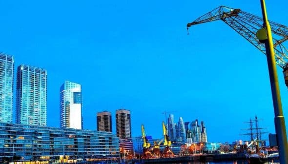 View of the Puerto Madero waterfront in Buenos Aires featuring modern buildings and a crane. - Olive Oil Times