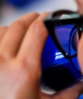 Individual holding a blue glass while taking a sip, partially visible from the side. - Olive Oil Times