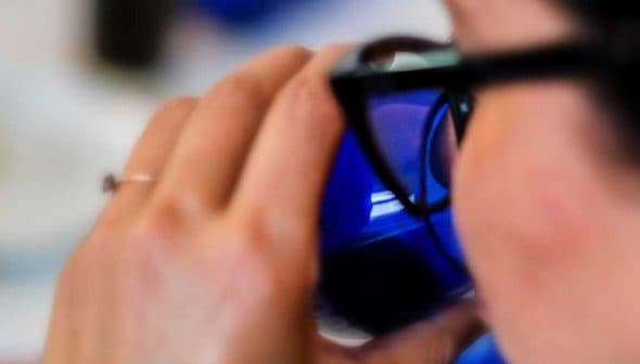 Individual holding a blue glass while taking a sip, partially visible from the side. - Olive Oil Times