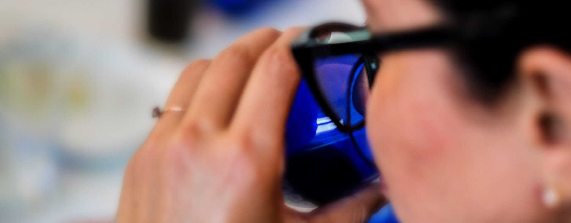 Individual holding a blue glass while taking a sip, partially visible from the side. - Olive Oil Times
