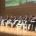 A panel of speakers seated on stage during a conference event, discussing various topics. - Olive Oil Times