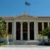 Facade of the University of Athens building with Greek flag and palm trees in front. - Olive Oil Times
