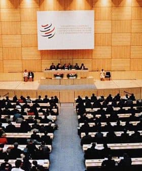 Interior view of a large conference hall during a World Trade Organization meeting with attendees seated. - Olive Oil Times