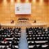 Interior view of a large conference hall during a World Trade Organization meeting with attendees seated. - Olive Oil Times