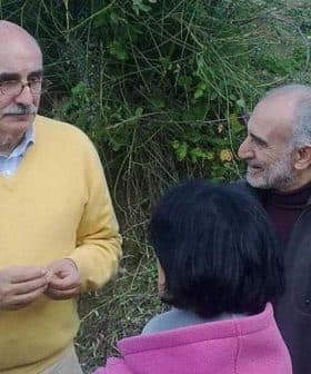 A man wearing a yellow sweater speaking to a small group of people outdoors. - Olive Oil Times